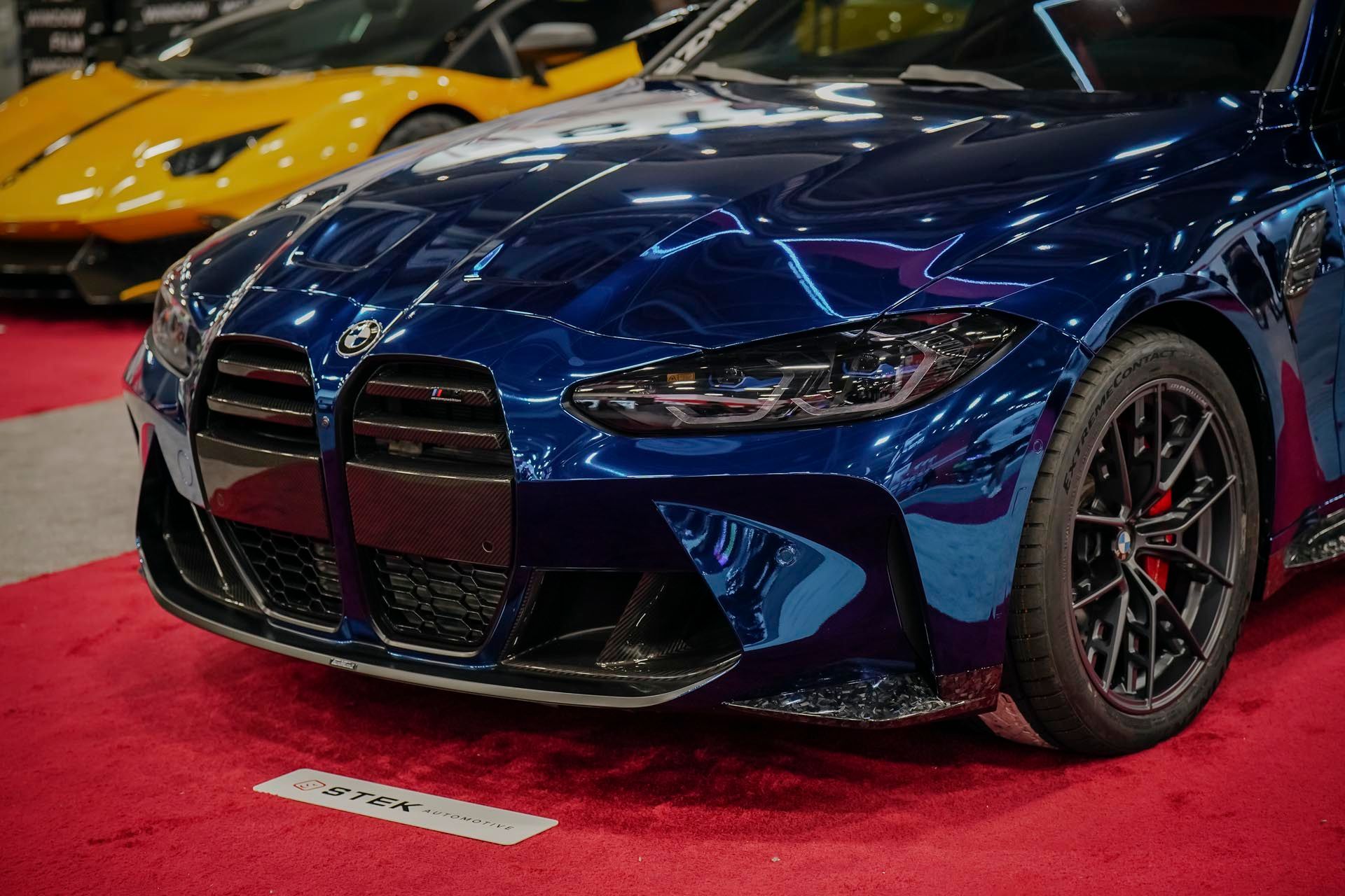 A blue car is parked on a red carpet next to a yellow car.