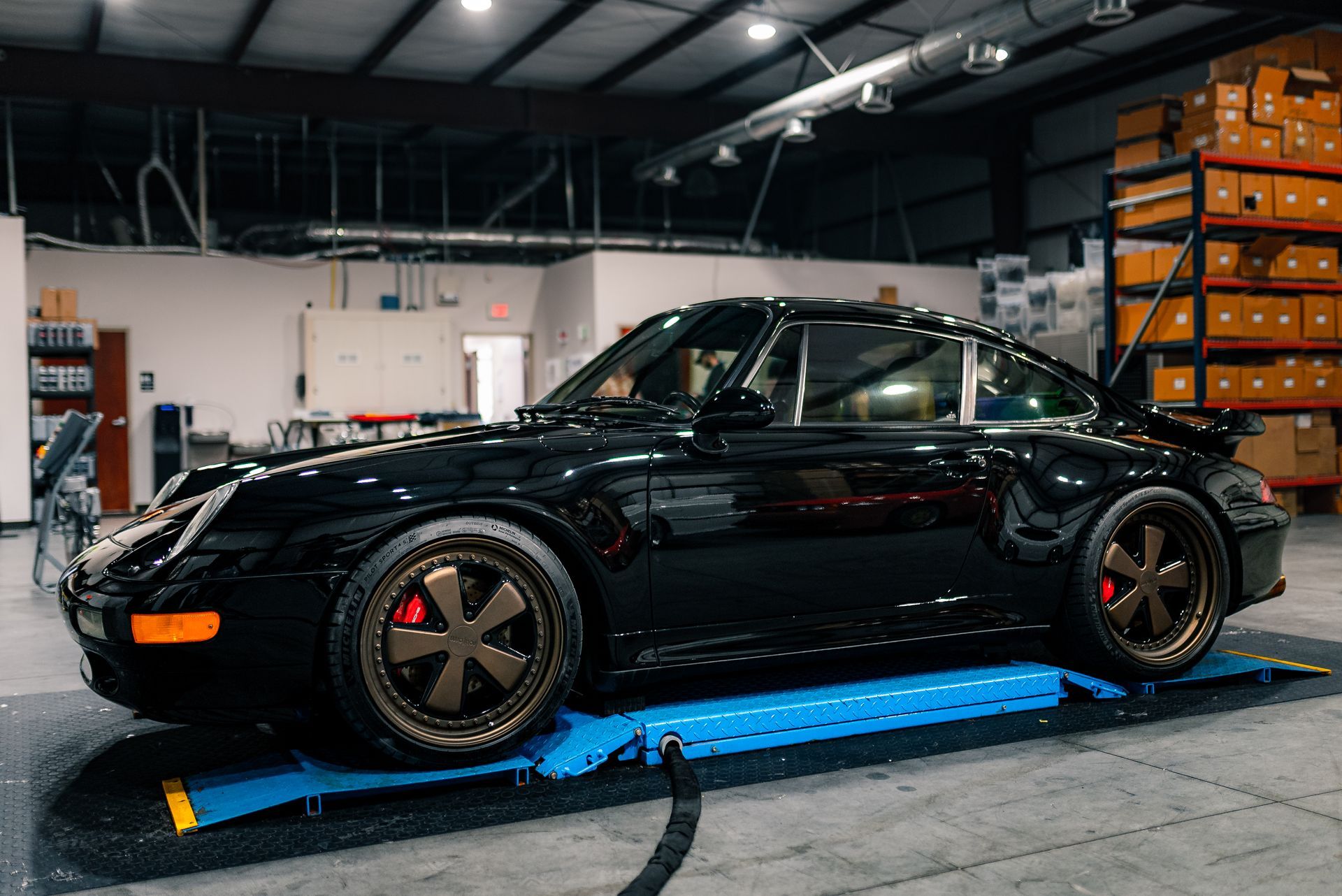 A black porsche 911 is parked on a lift in a garage.