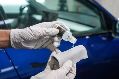 A person is applying a coating to a blue car.