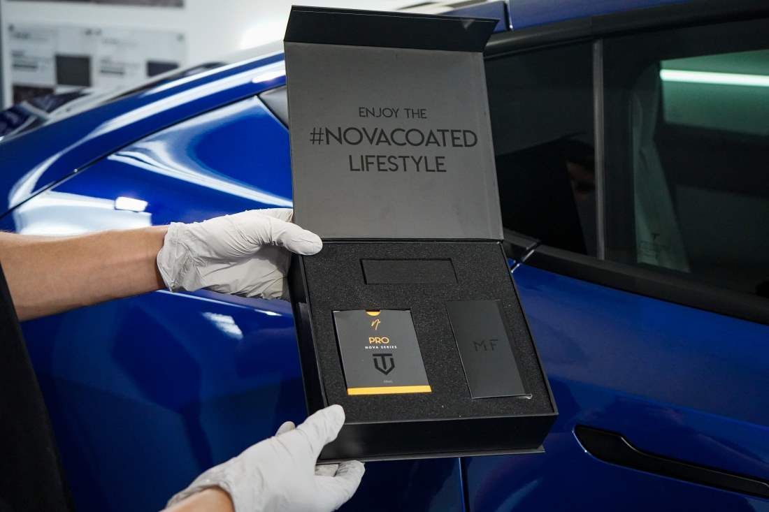 A person is holding a box in front of a blue car.