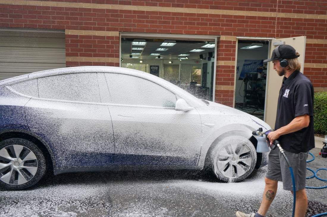 A man is washing a tesla model y with foam.