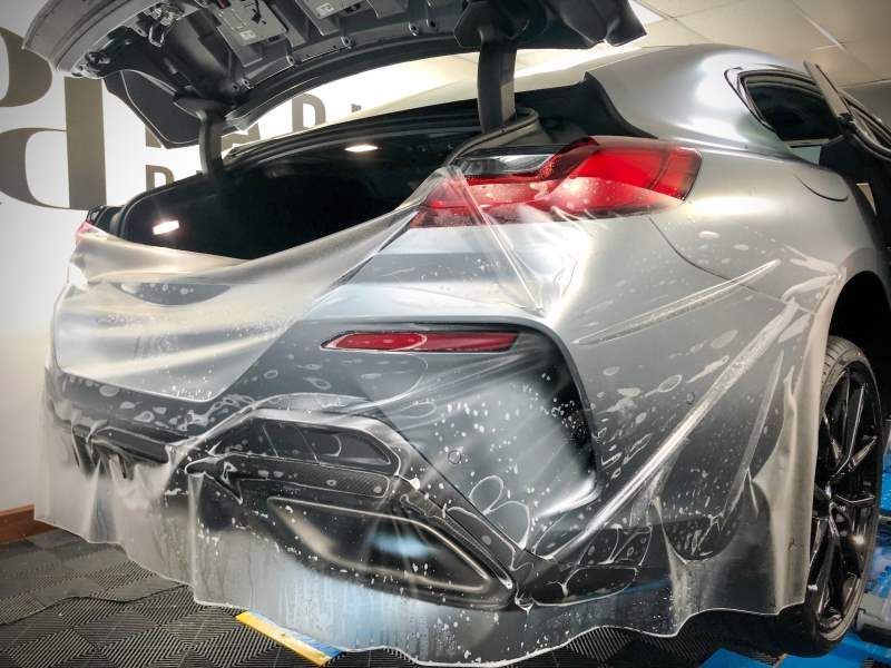 A silver car is wrapped in plastic and has the trunk open.