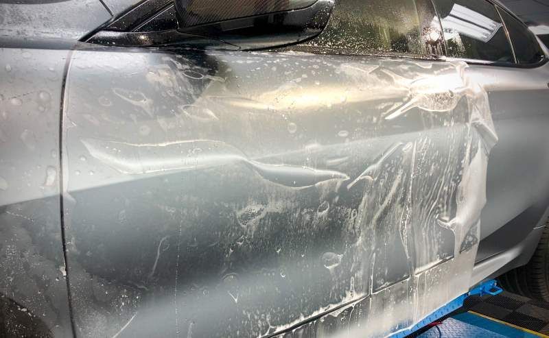 A car is covered in plastic wrap and is sitting on a lift.