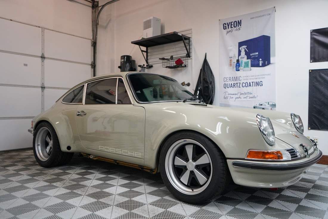 A white porsche is parked in a garage next to a garage door.