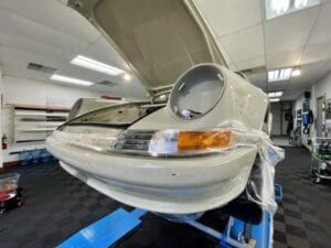 A white car with the hood up is sitting on a lift in a garage.