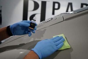 A person wearing blue gloves is cleaning a car with a cloth.