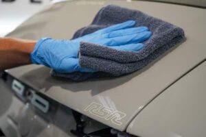 A person wearing blue gloves is cleaning a car with a towel.