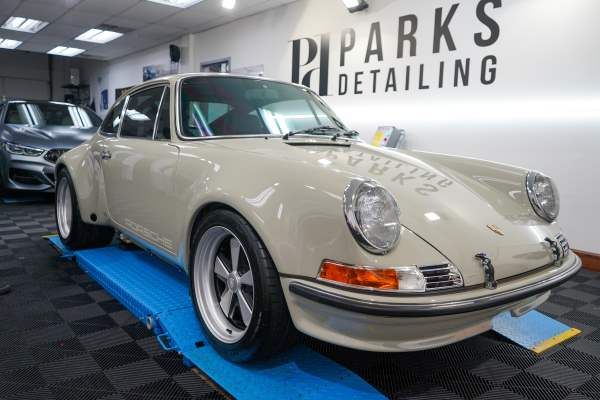 A white porsche is sitting on a blue lift in a showroom.