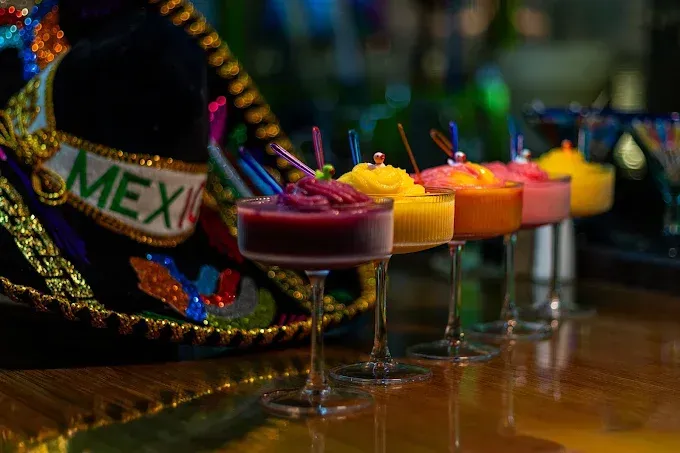 Colorful Mexican cocktails lined up beside a sombrero on a bar table
