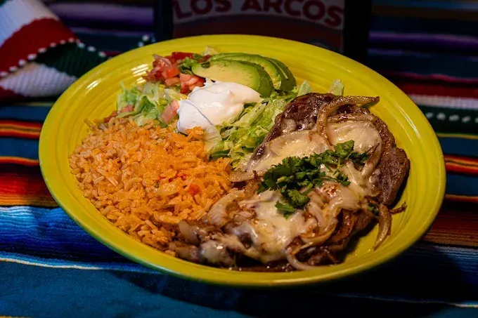 Mexican meal on a yellow plate with rice, salad, and cheesy chicken enchiladas on a colorful table