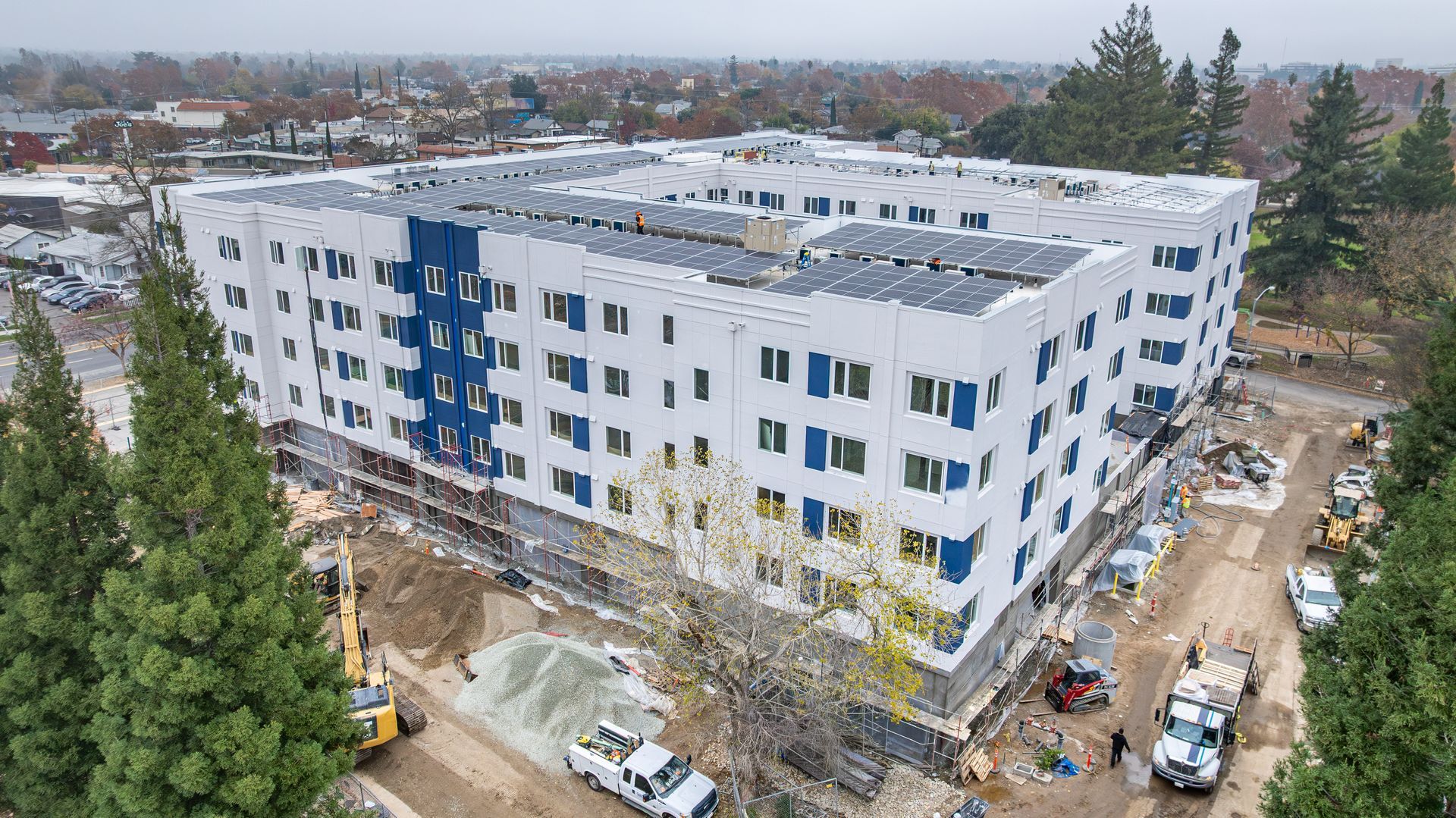 Aerial view of a white apartment building with blue accents under construction in a suburban area