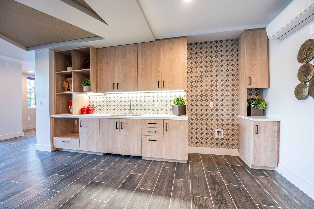 Modern kitchen with light wood cabinets, patterned backsplash, white countertops, and dark tile floor
