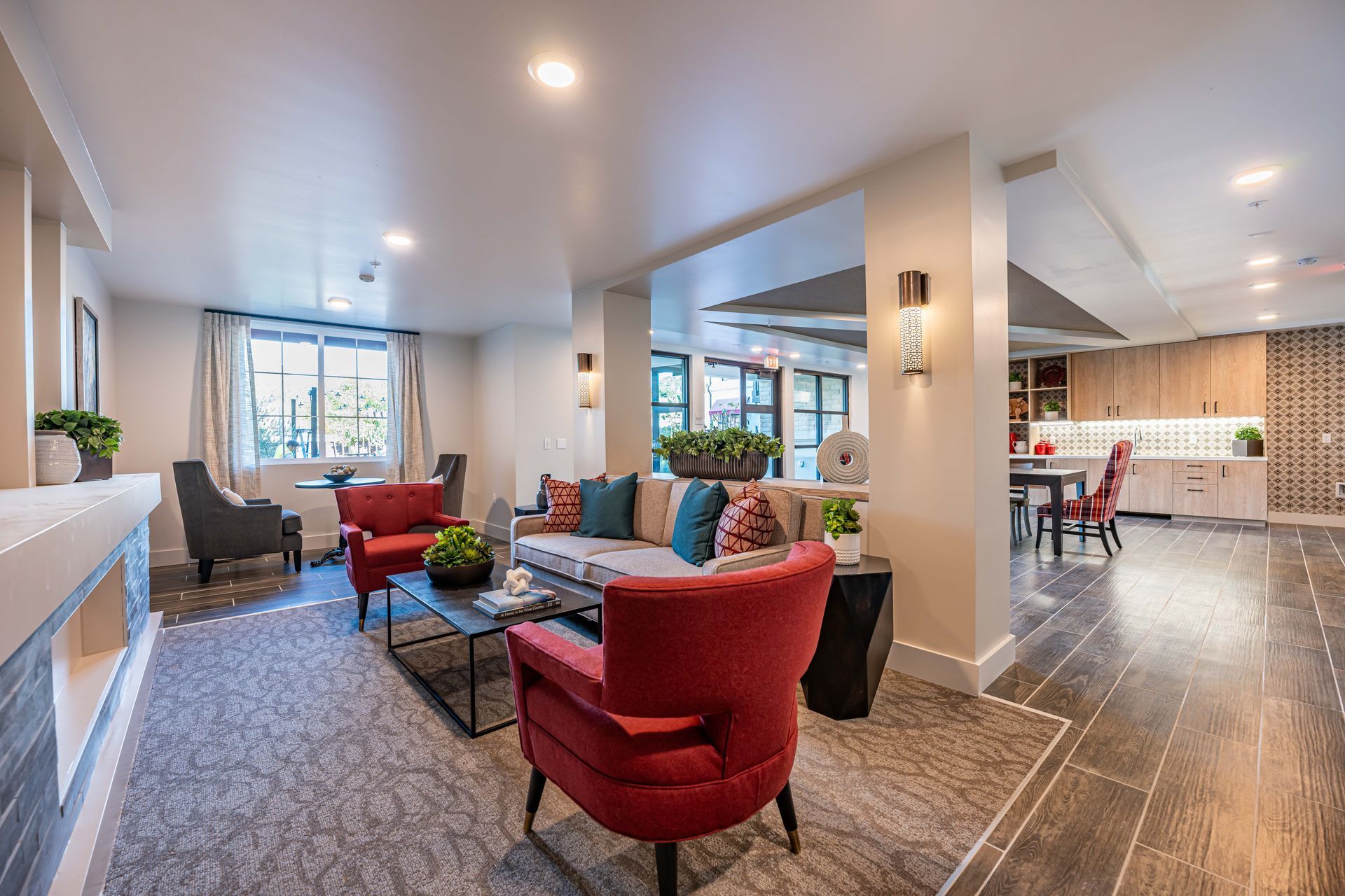 Bright open-concept living room with red chairs, gray sofa, kitchen, and large windows
