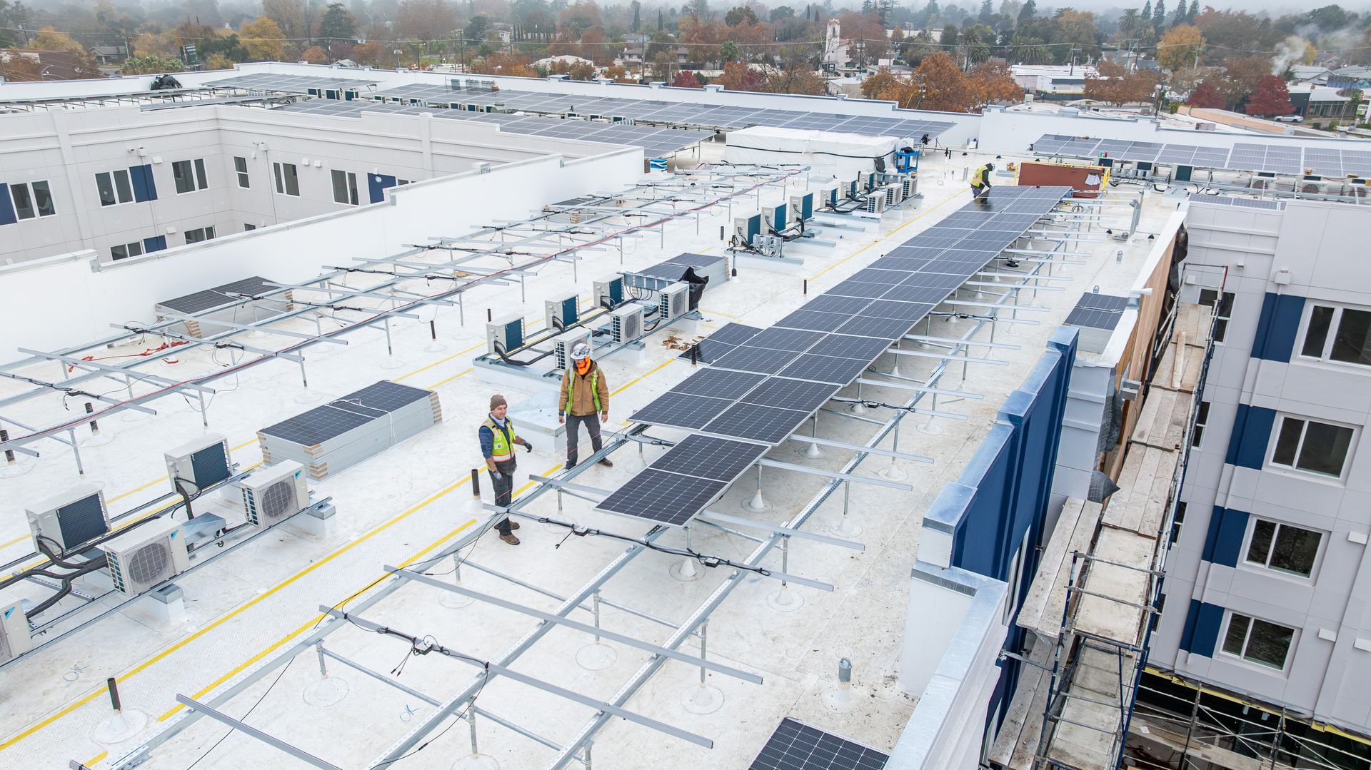 Workers installing solar panels on a snowy rooftop of a large building
