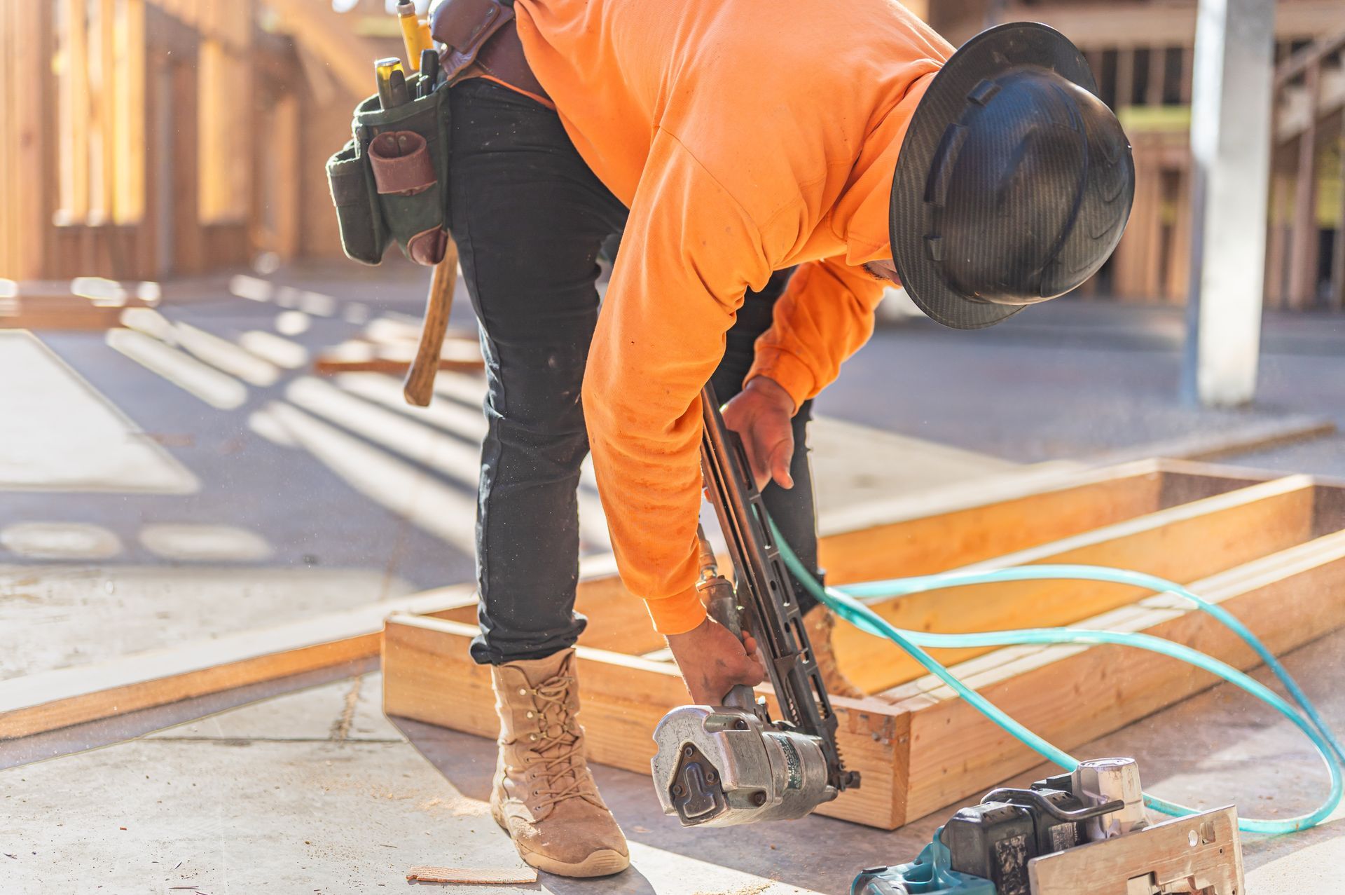 Worker in orange hoodie cuts wood with a circular saw at a construction site.