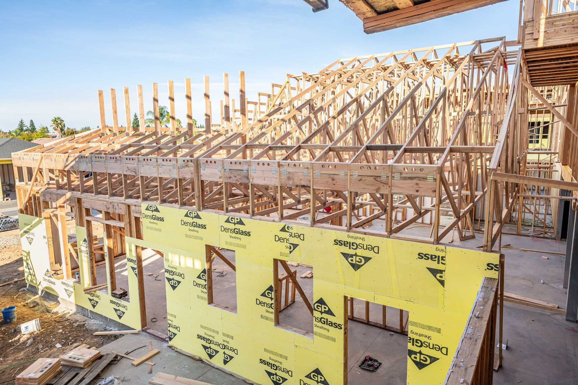Wood-framed house under construction with yellow wrap and exposed roof trusses