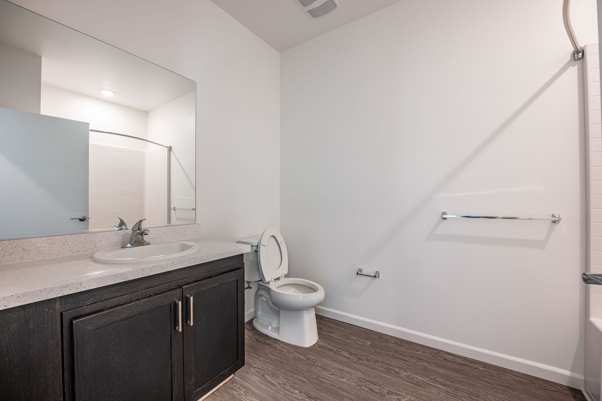Modern bathroom with vanity, mirror, toilet, and shower curtain on white walls and dark flooring
