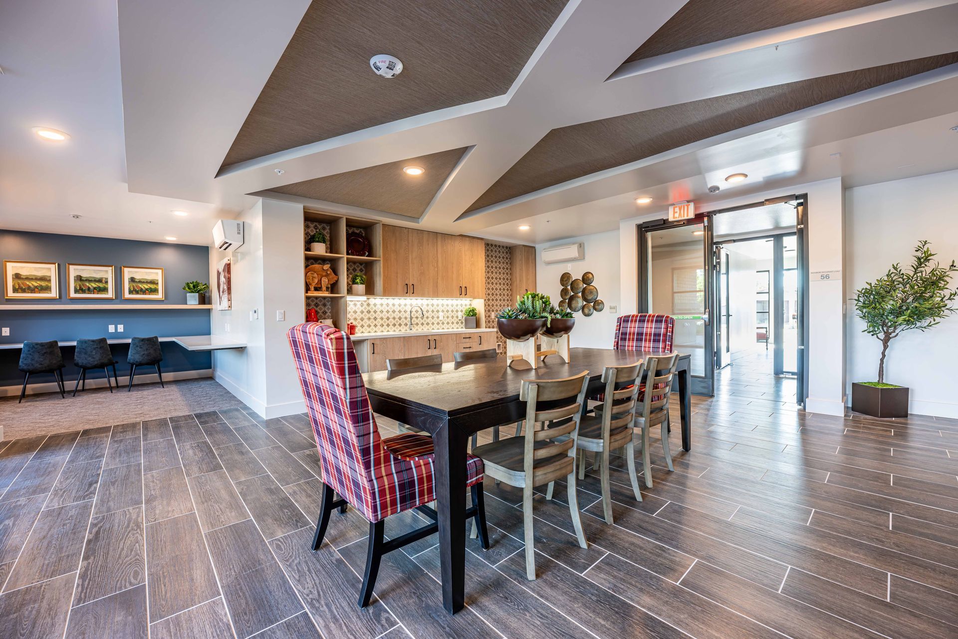 Modern dining room with long table, red patterned chairs, wood floor, and ceiling lights