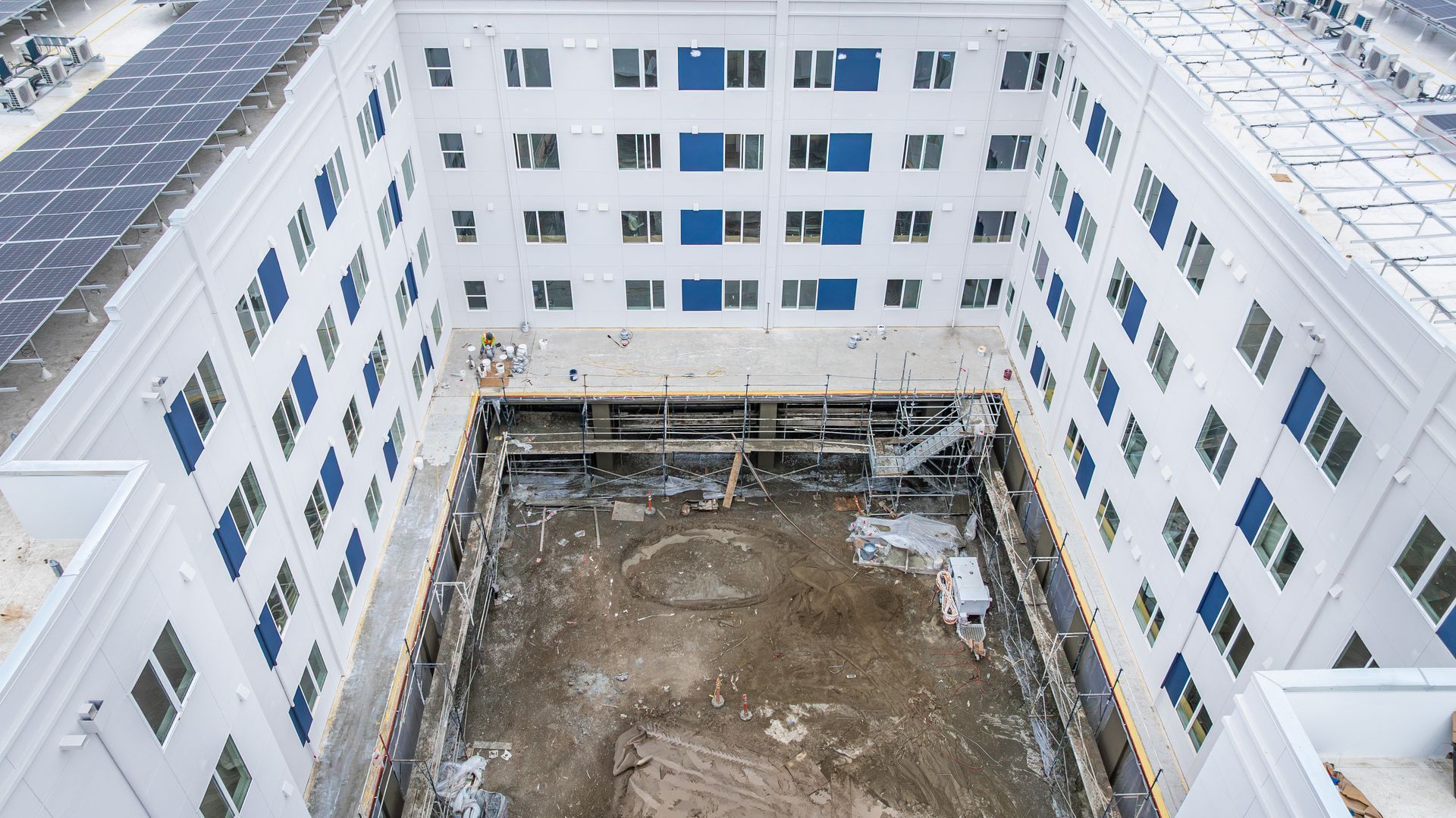 Courtyard of a white apartment building under construction, with a dirt lot in the center