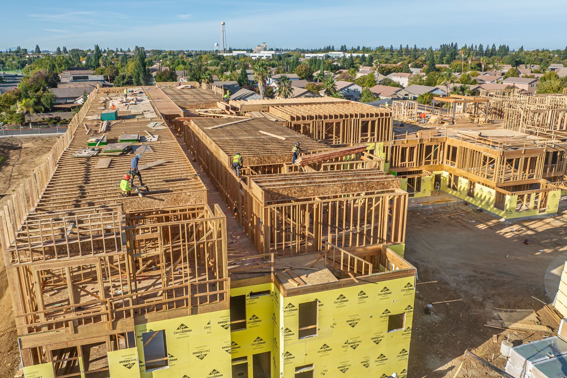 Aerial view of a large building under construction with wooden framing and yellow walls in a suburban area