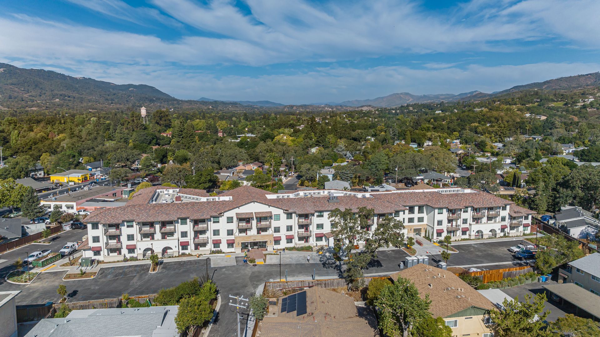 Aerial view of a white apartment complex in a green hillside neighborhood under a blue sky