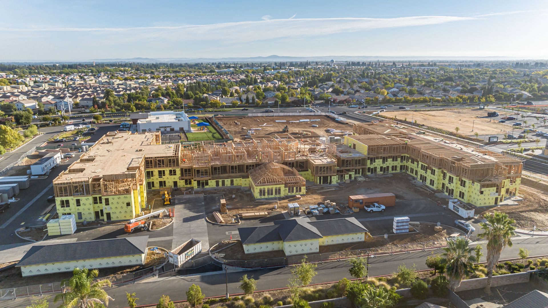 Aerial view of a large tan apartment complex with parking lots in a suburban neighborhood.