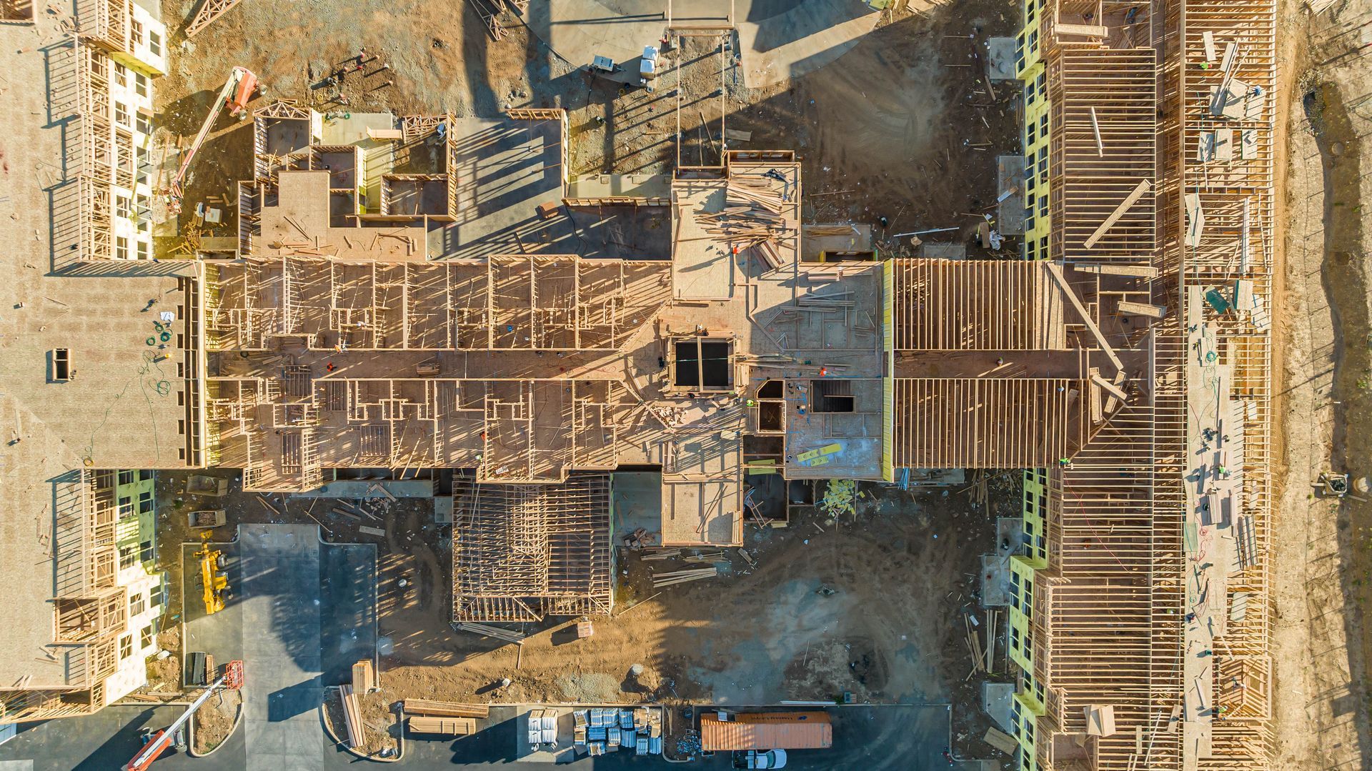 Aerial view of a dusty construction site with wooden scaffolding, foundations, and workers below