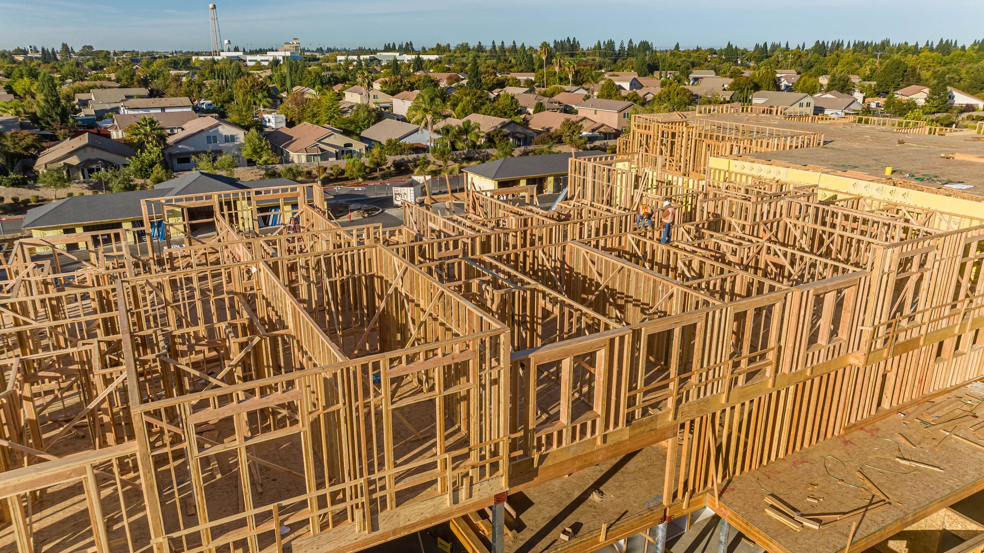 Wood-framed houses under construction in a suburban neighborhood, viewed from above at sunset.