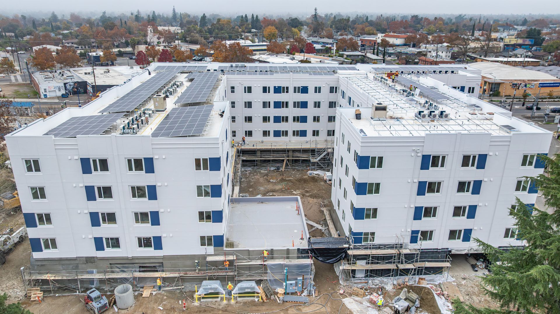 Aerial view of a snowy apartment complex under construction with surrounding trees and houses