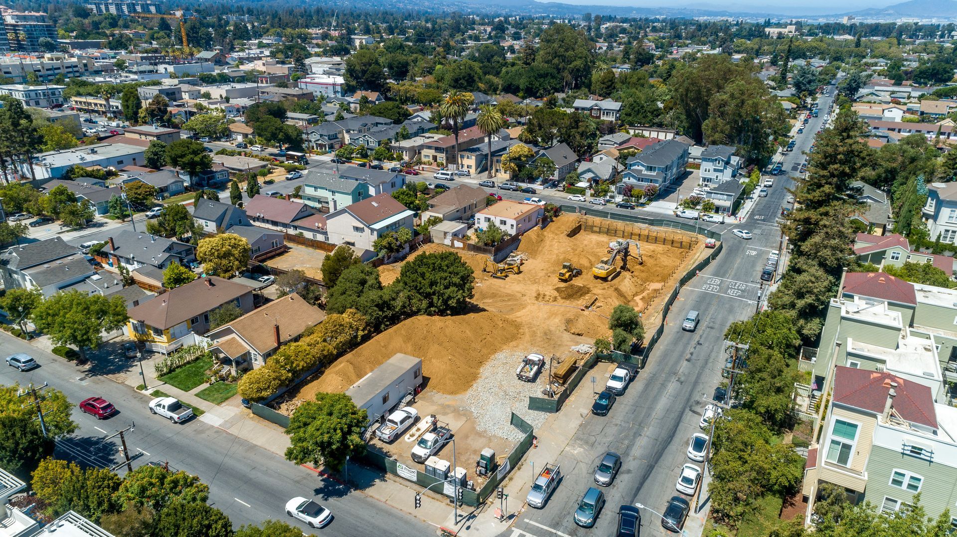 Aerial view of a suburban neighborhood with houses, a vacant lot, and traffic on a busy street.