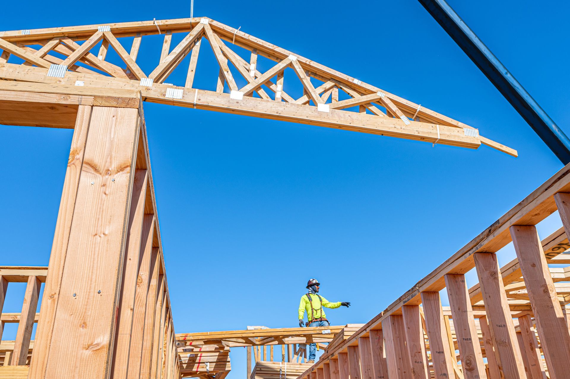Framed house under construction with a worker on the roof trusses against a blue sky