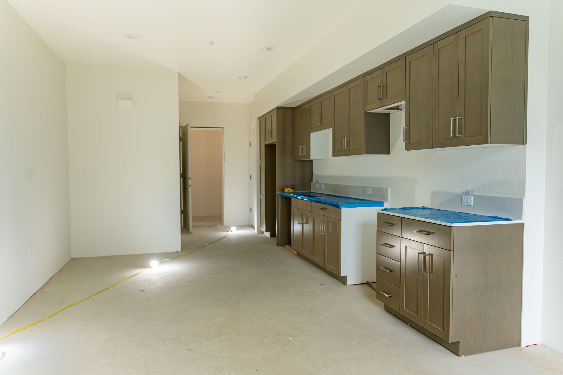 Empty kitchen with brown cabinets, blue countertop covering, and unfinished floor in a bright room