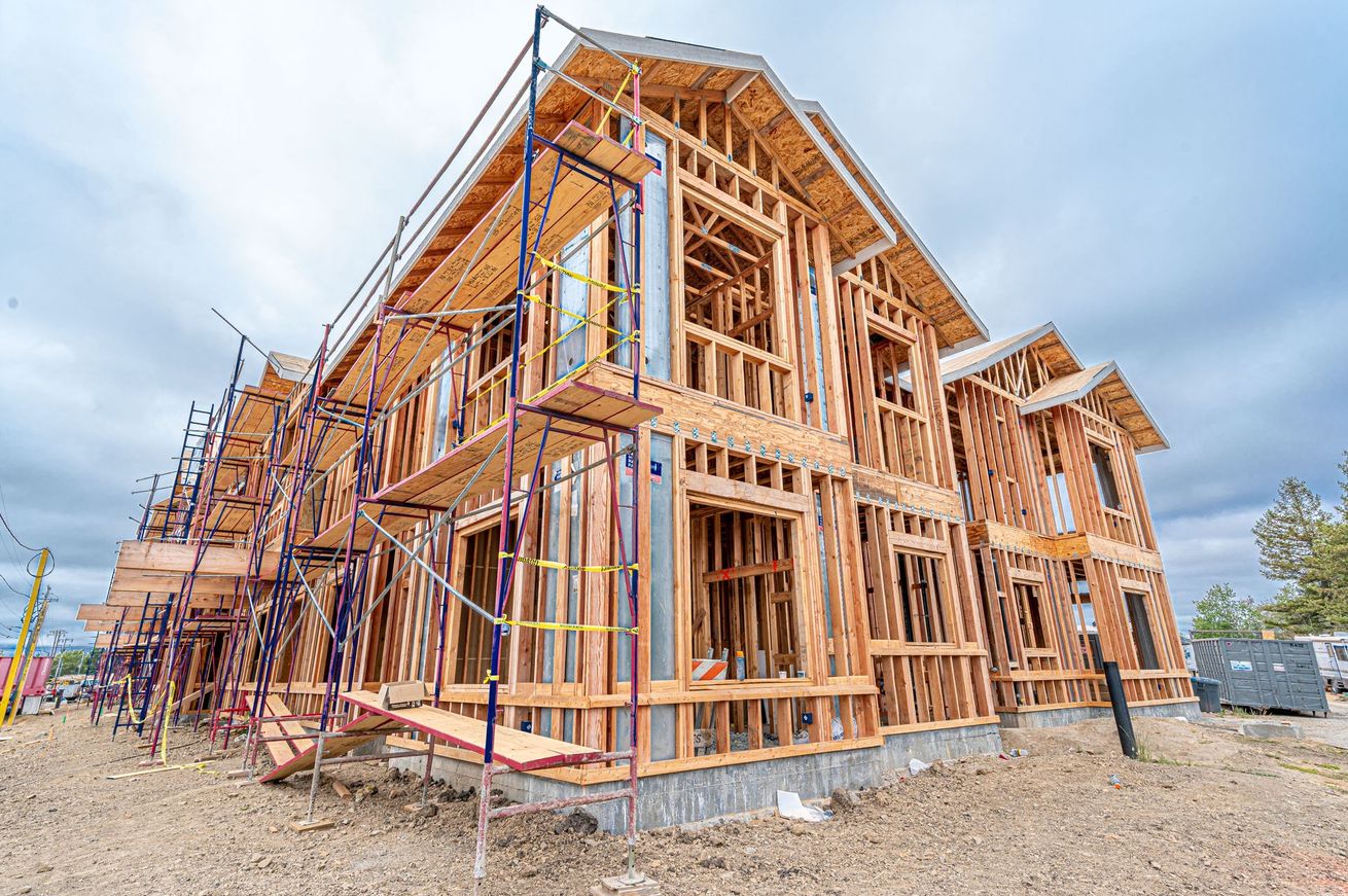 Partially built wooden house framed with scaffolding on a construction site under a cloudy sky