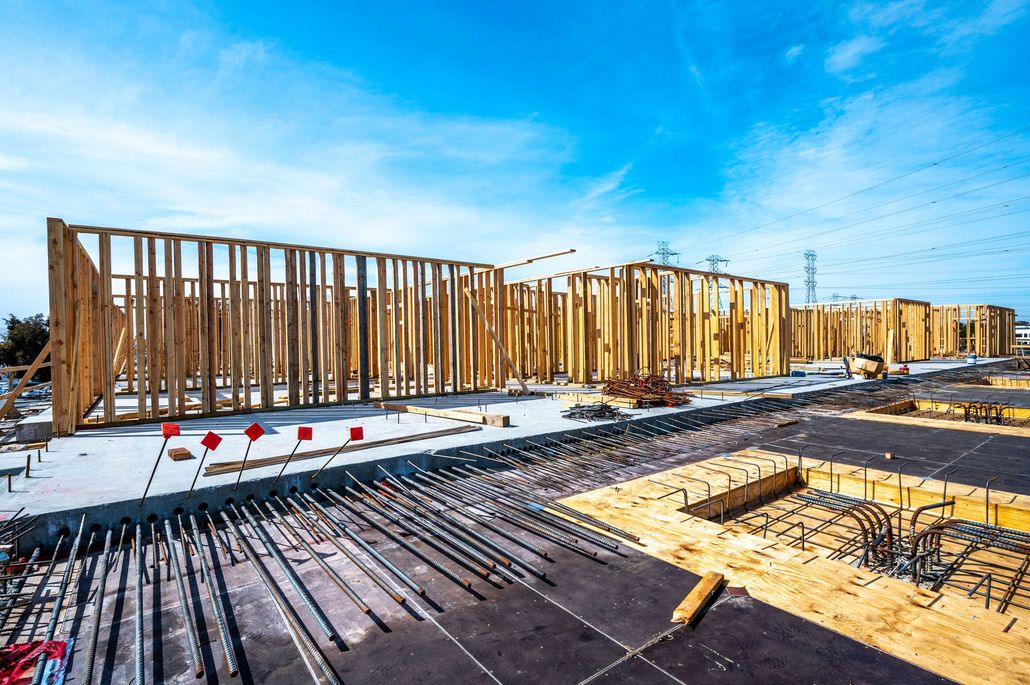 Wooden house framing under construction with rebar, snow on the ground, and a clear blue sky