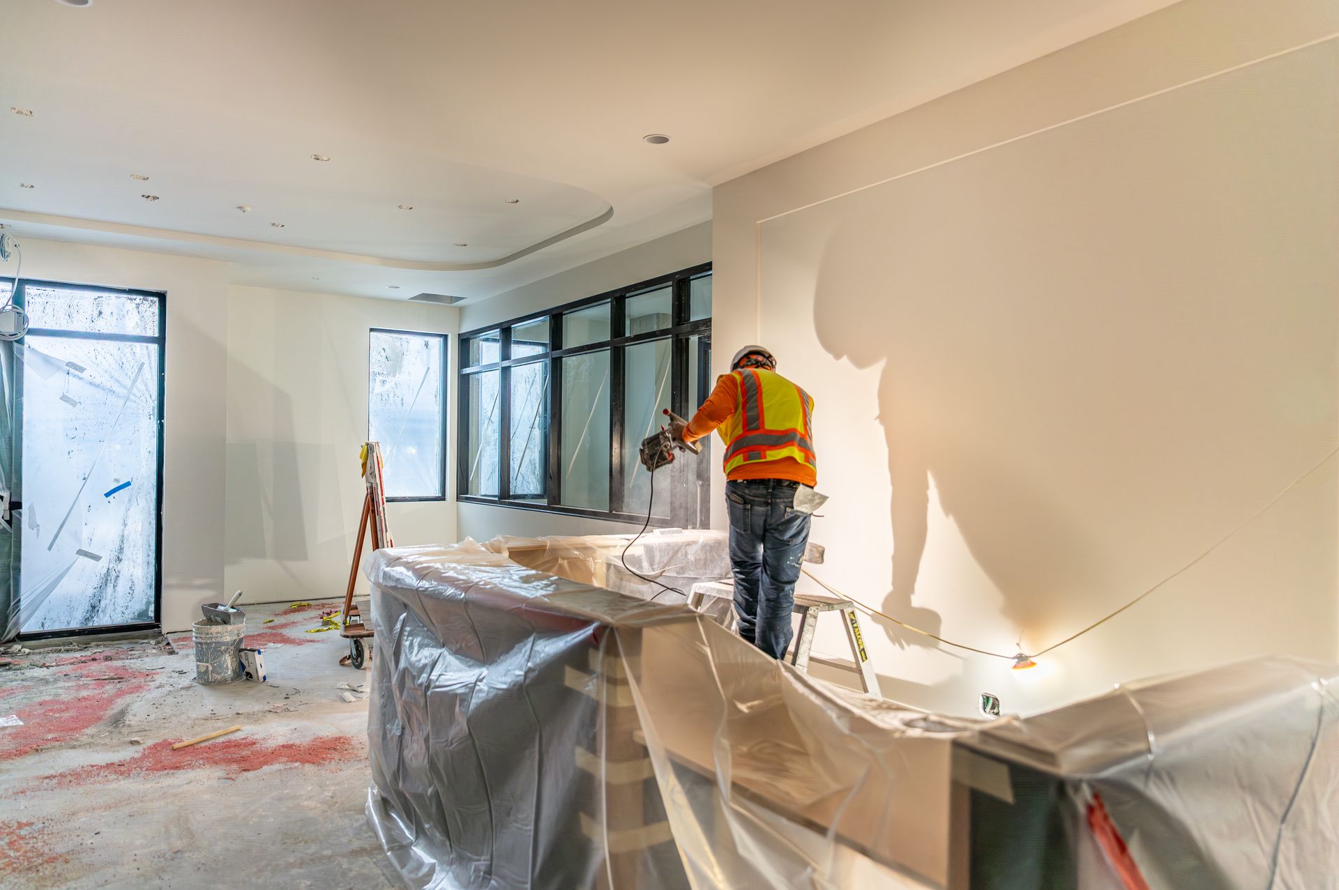 Worker painting a bright apartment interior, with plastic-covered floors and windows during renovation