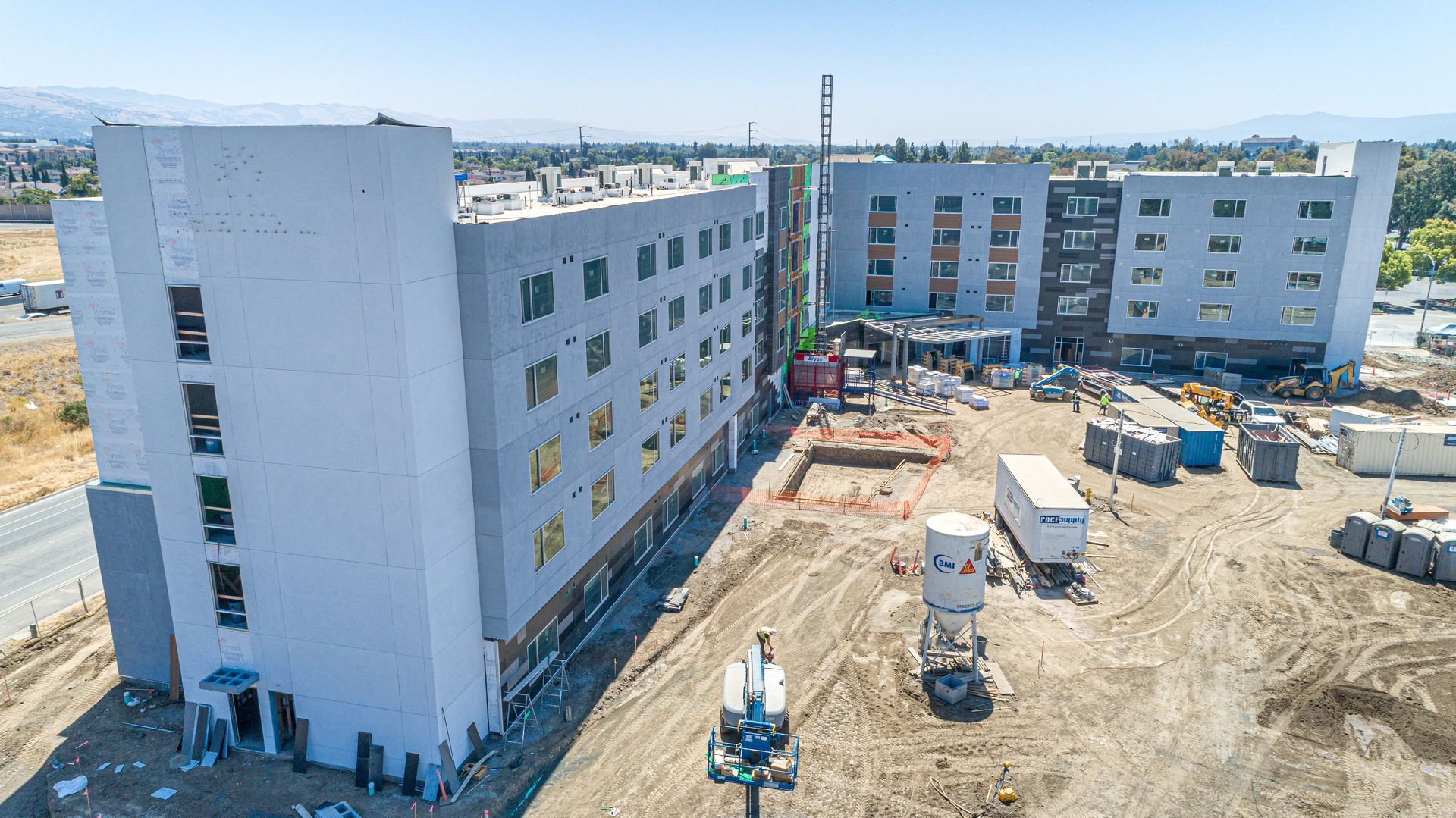 Aerial view of a construction site with white apartment buildings and heavy equipment on a dirt lot.