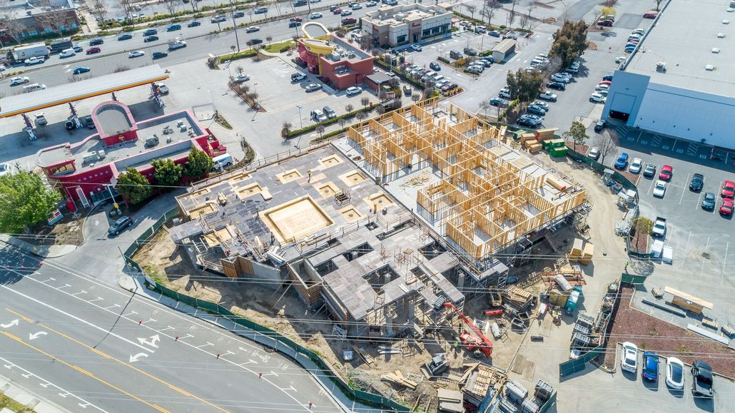 Aerial view of a construction site beside a parking lot and commercial buildings