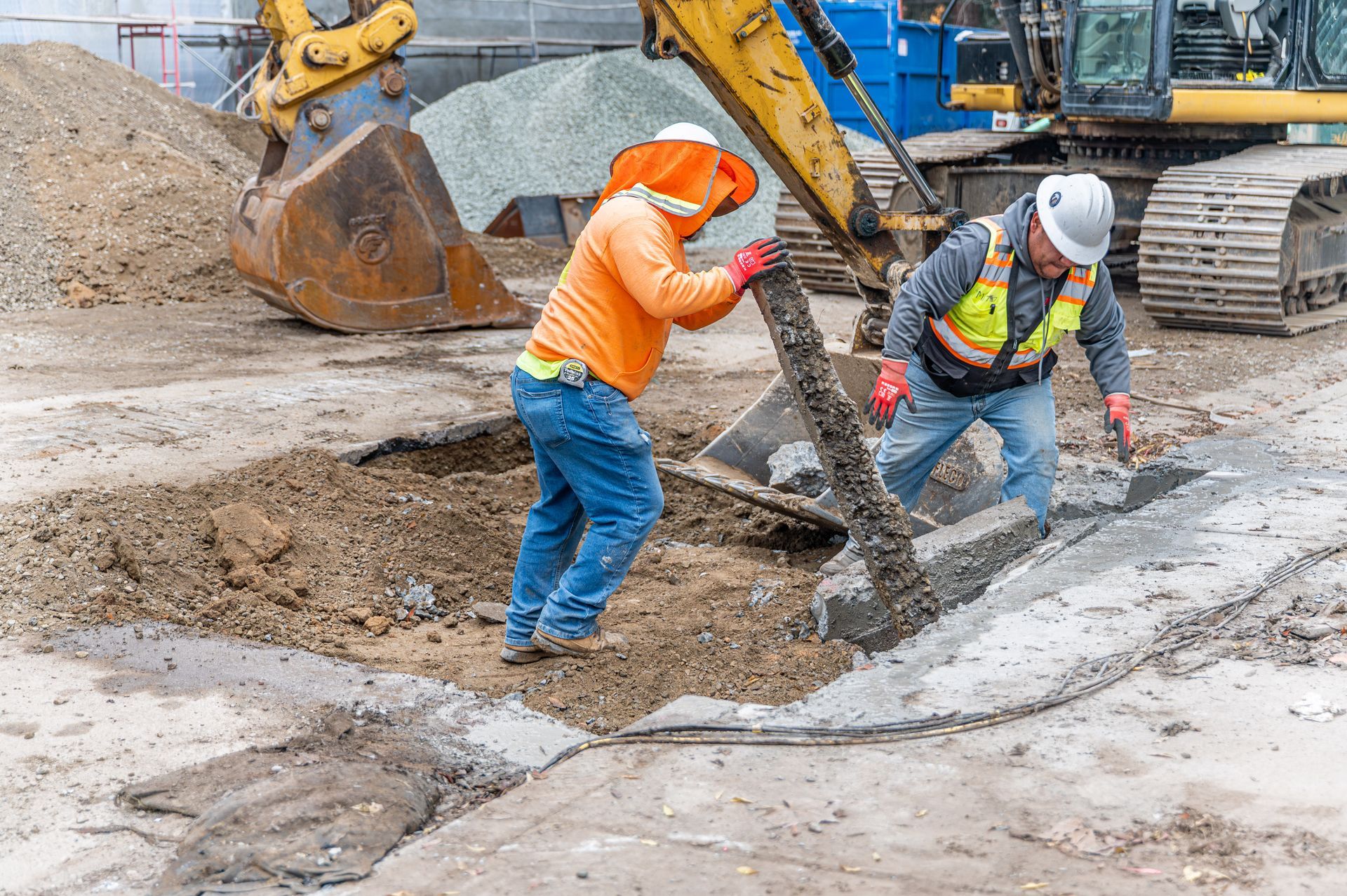 Construction workers in hard hats repairing a concrete trench beside an excavator