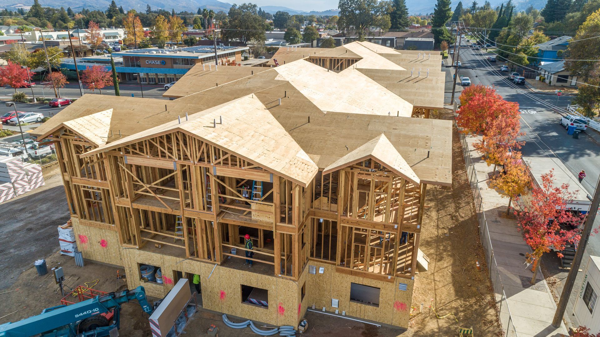 Wood-framed houses under construction with multiple rooflines and plywood sheathing on a sunny day
