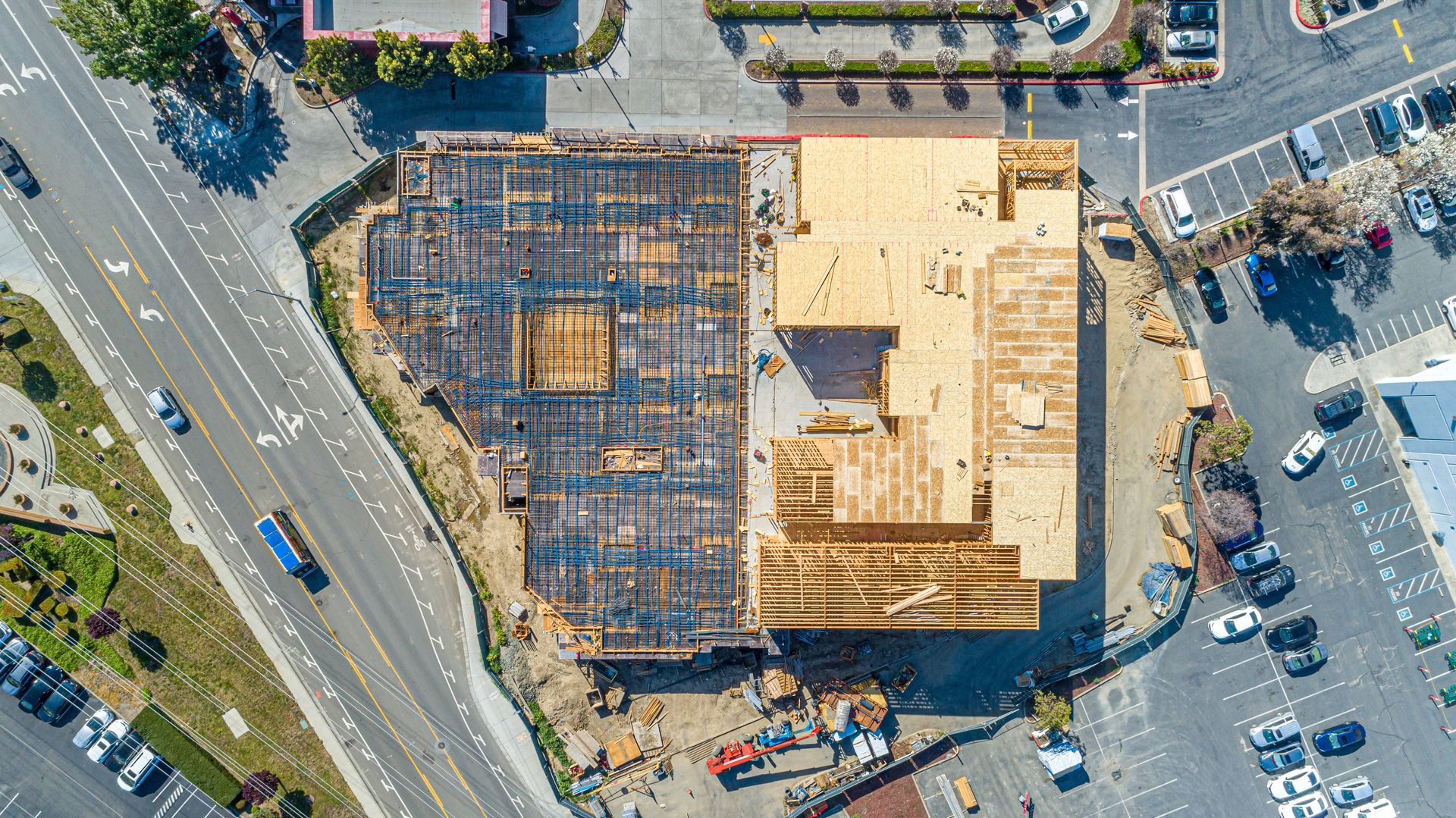 Aerial view of a construction site with concrete foundation, rebar, and surrounding parked cars and roads