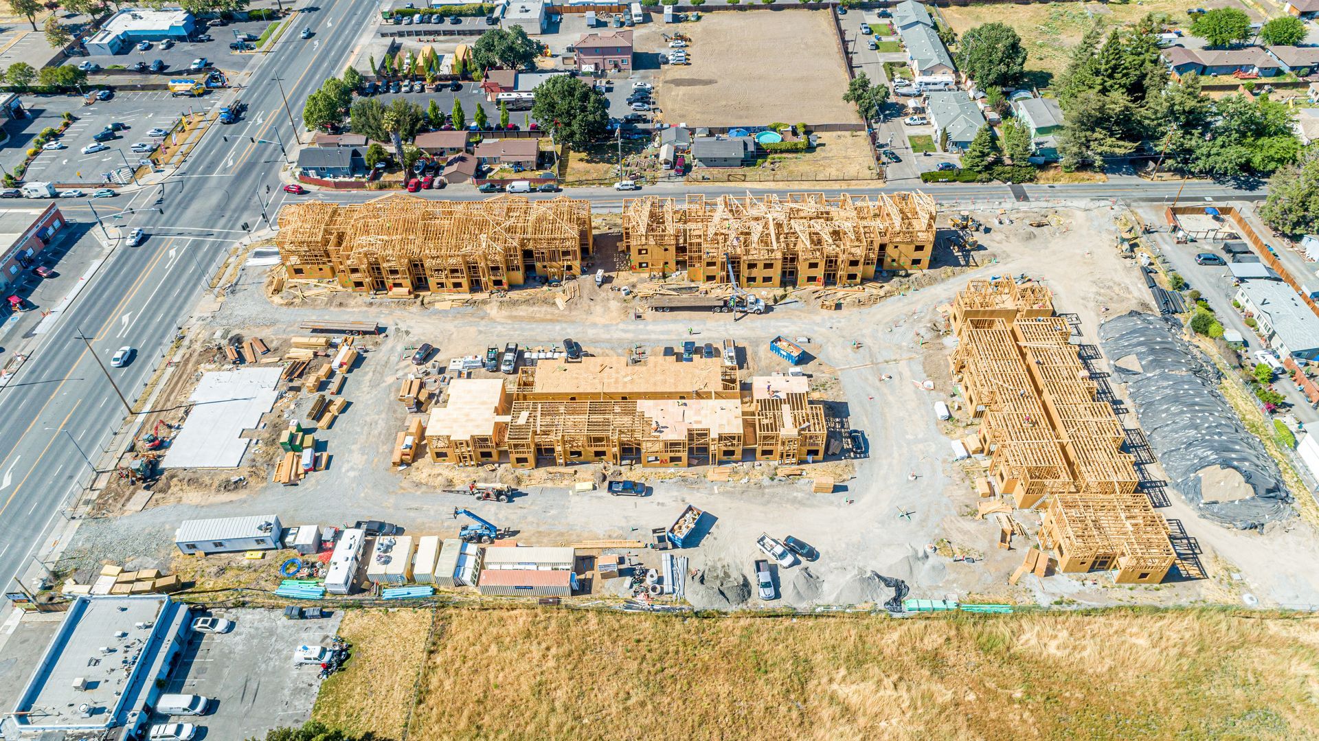 Aerial view of a residential construction site with rows of wooden house frames beside a main road.