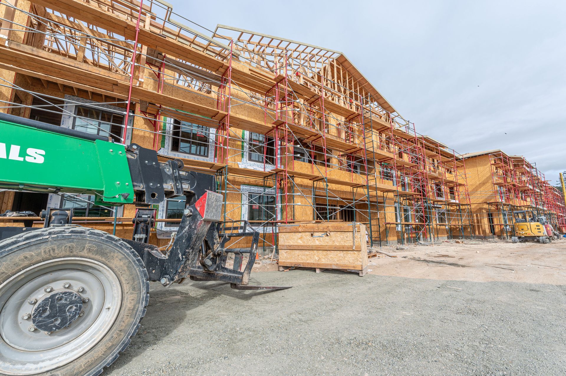 Construction site with orange scaffolding, green lift, and partially built wooden structures.