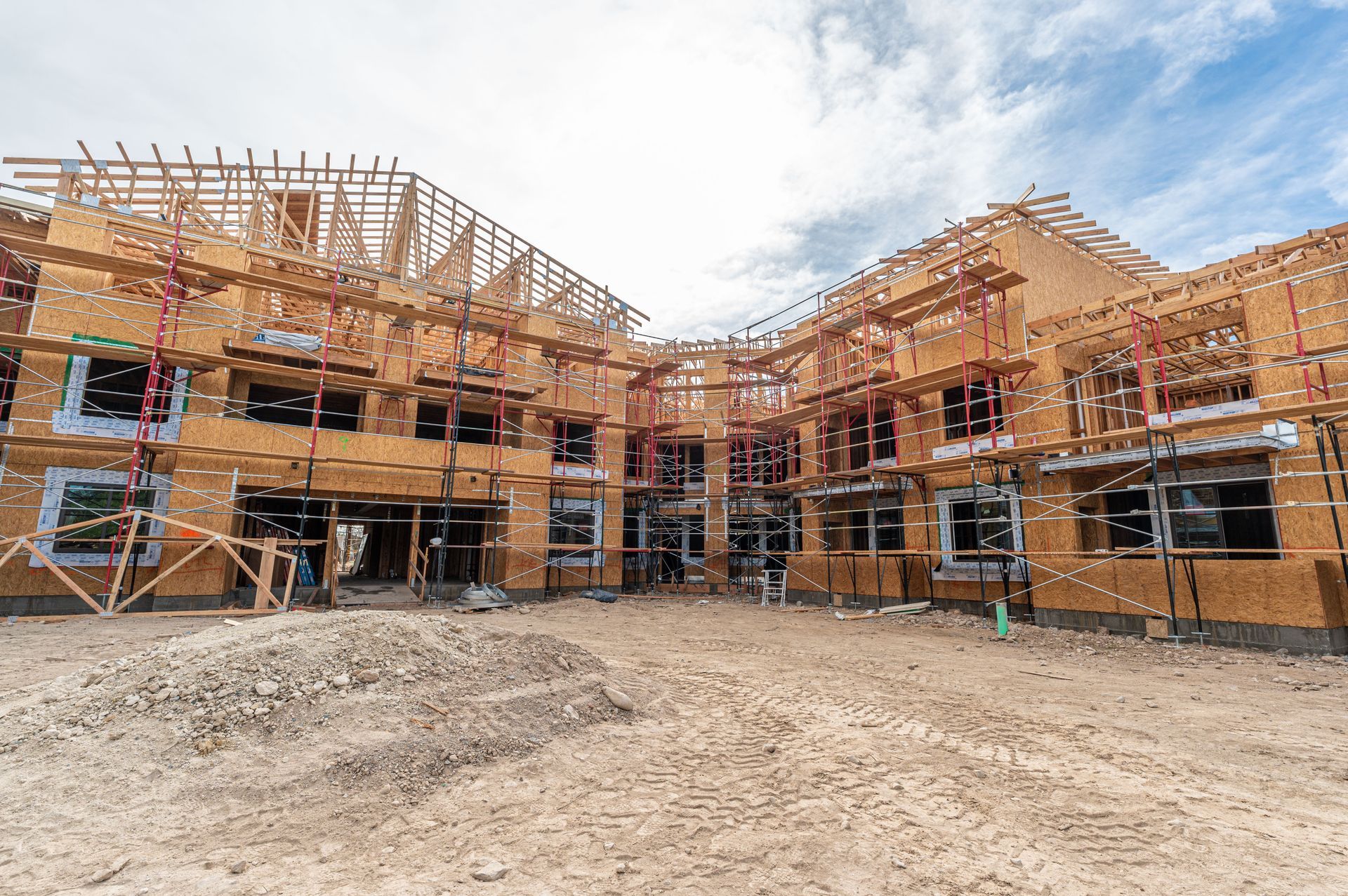 Large brick apartment building under construction with scaffolding and a dirt lot in front