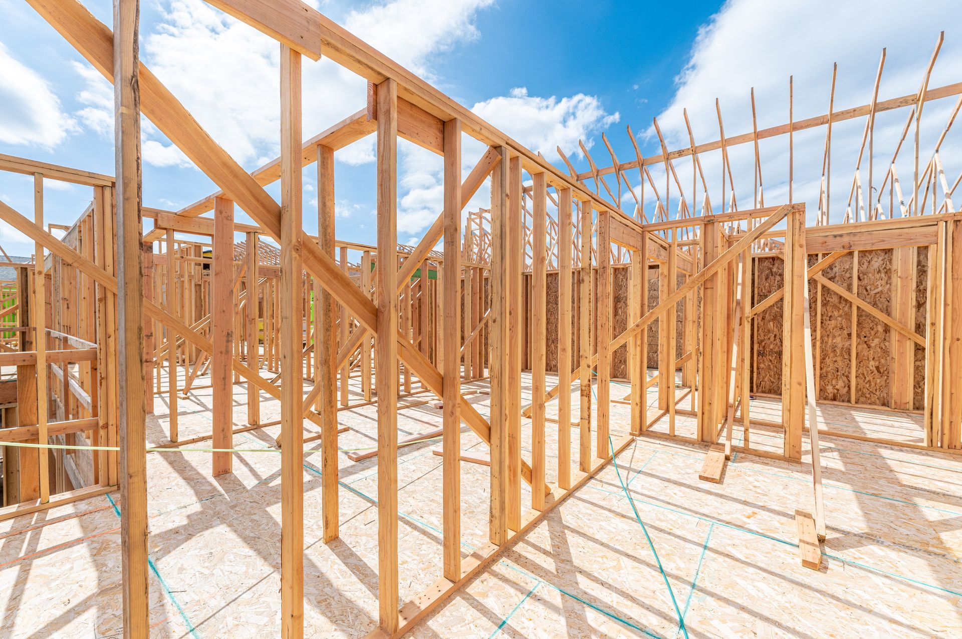 Wood-framed house under construction with exposed studs against a blue sky.