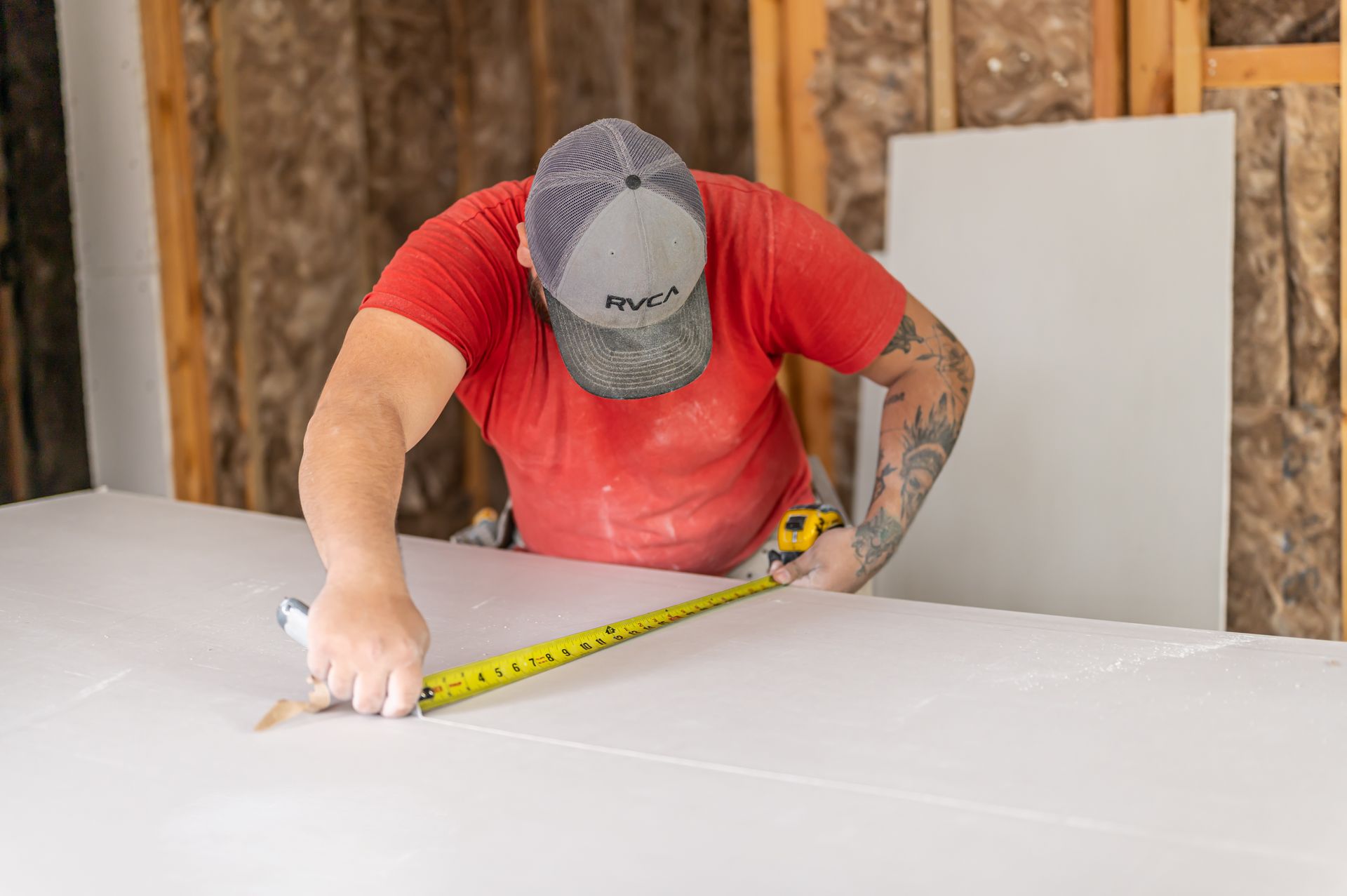 Two construction workers wearing high-visibility vests and safety gloves examine a set of building plans.