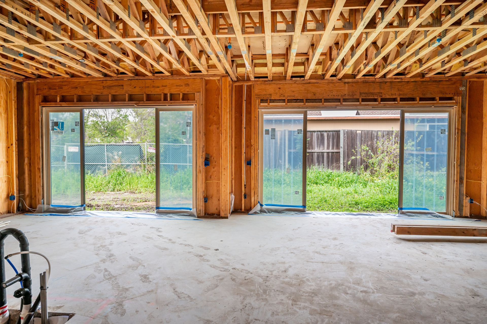 Unfinished room interior with exposed framing, sliding glass doors, and a concrete floor under construction