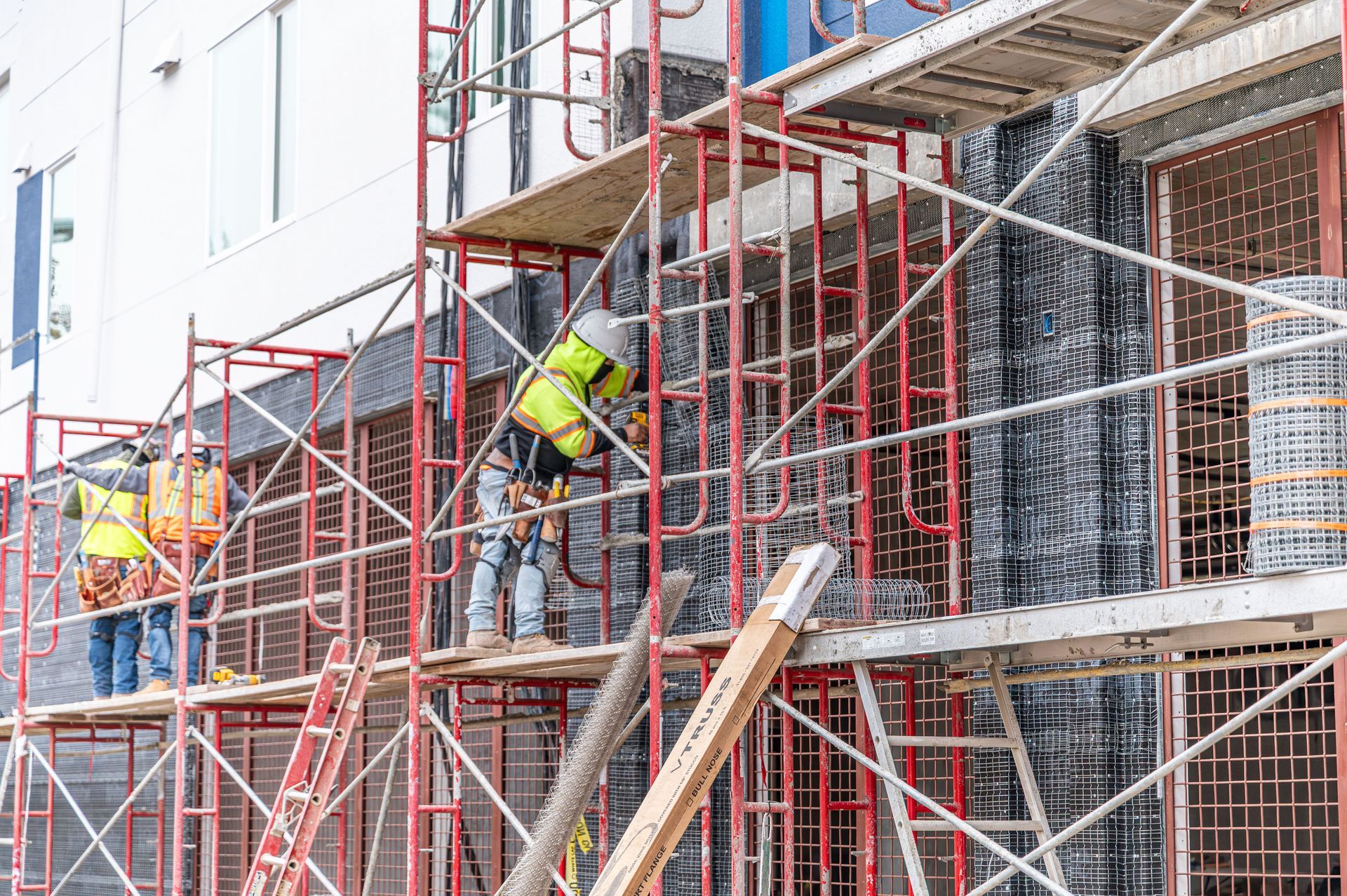 Construction workers on red scaffolding repairing a building exterior with safety harnesses
