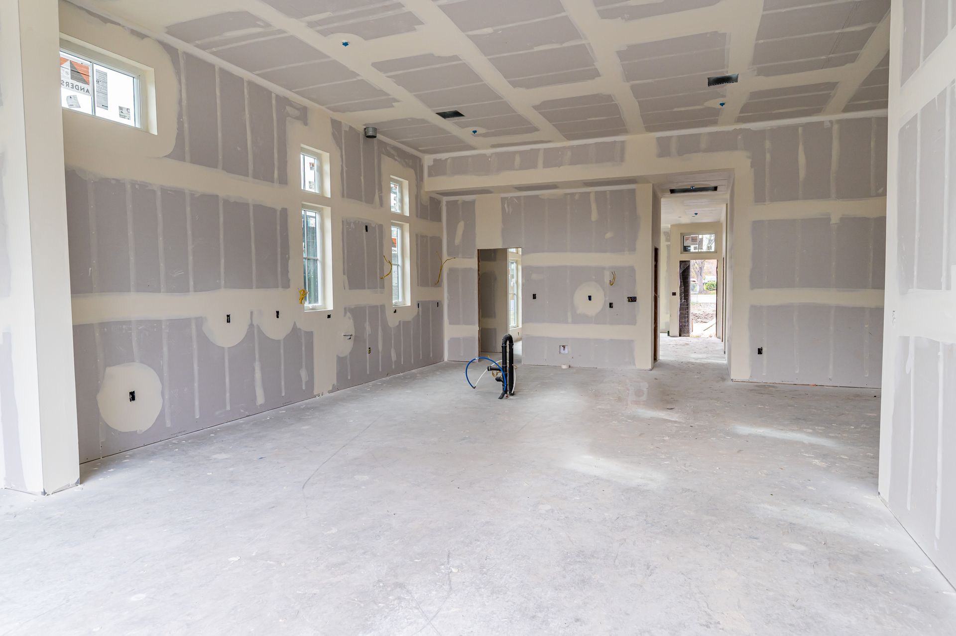 Unfinished drywall room with windows, white walls, and a concrete floor during construction.