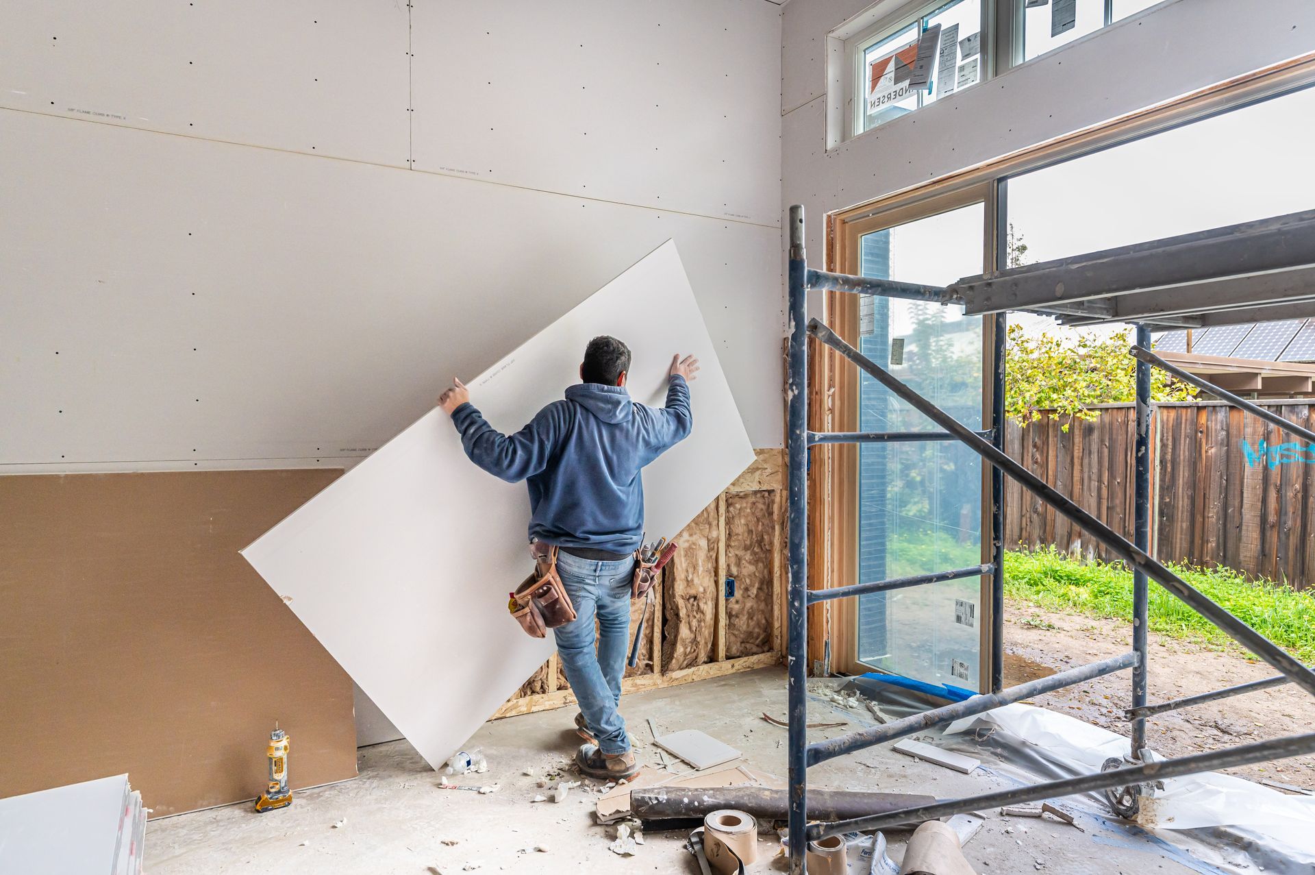 Worker installing a large white panel on an unfinished interior wall near scaffolding