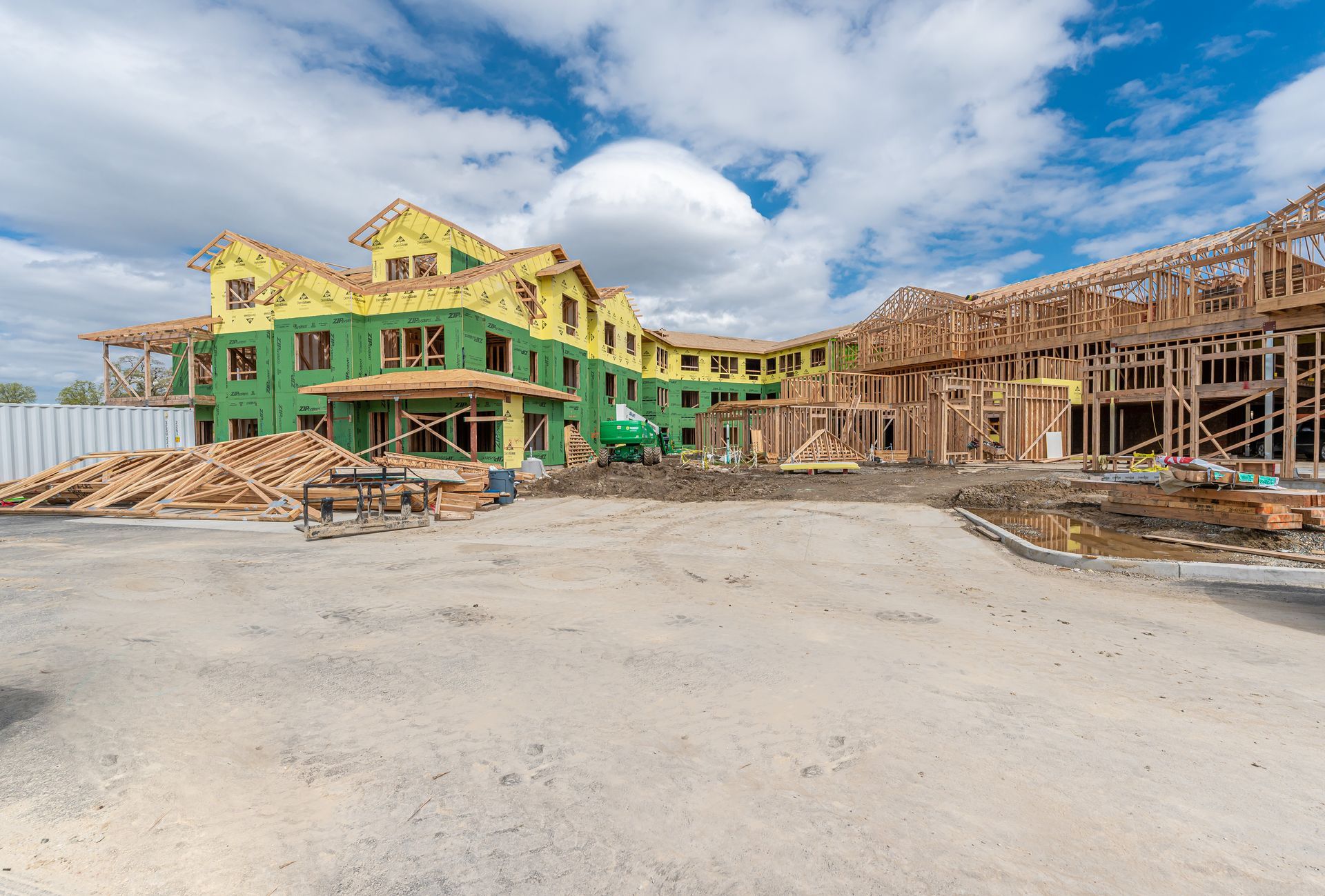 Partially built homes at a construction site with green sheathing and wooden framing under a cloudy sky